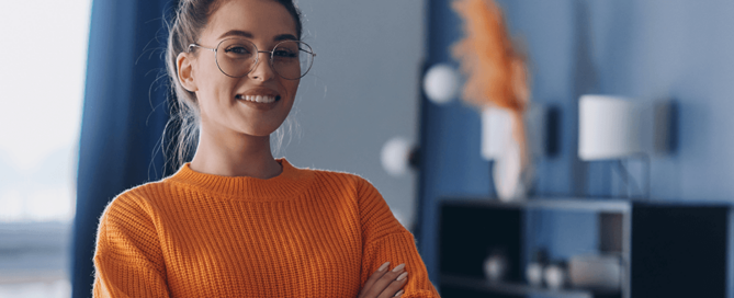 Attraktive junge Frau mit Brille und orangenem Pullover