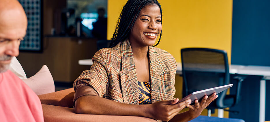 Smiling businesswoman in a plaid blazer holding a tablet in a modern office. Empowerment and professional growth