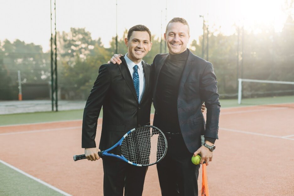 Zwei Manager eines Tennisvereins posieren vor einem Tennisplatz