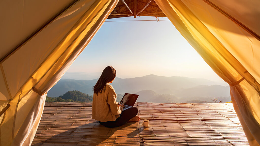 Work and Travel: Frau sitzt vor Zelt und schreibt auf dem Laptop